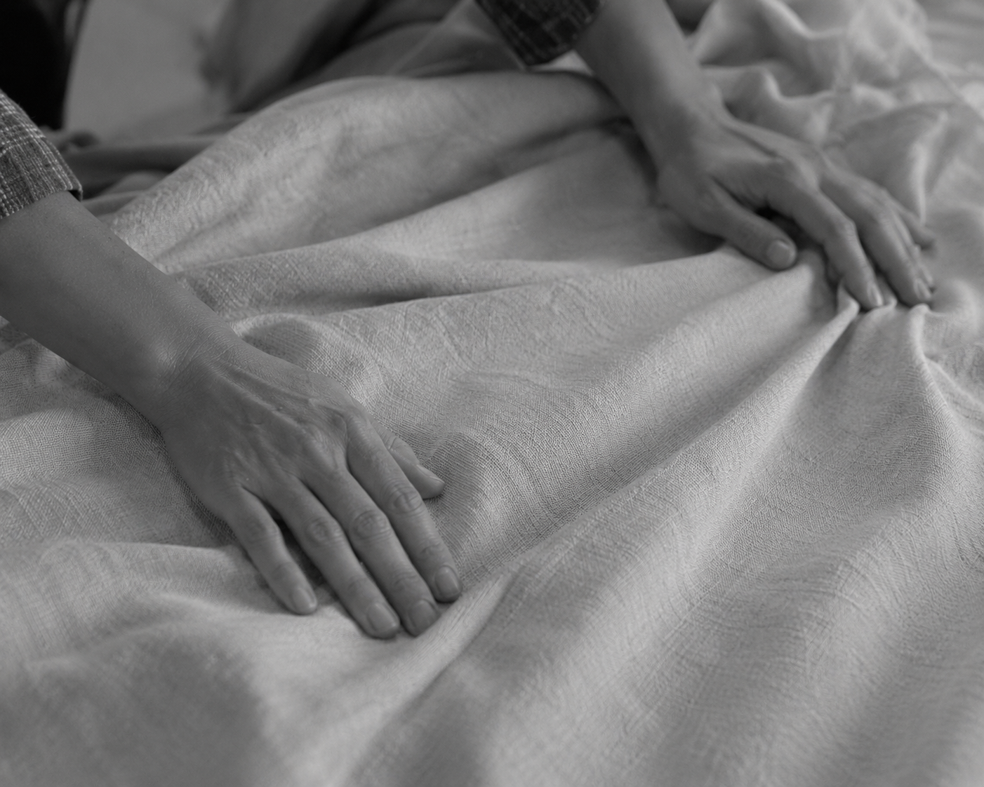 Two hands smoothing a textured woven throw on a bed, in black and white