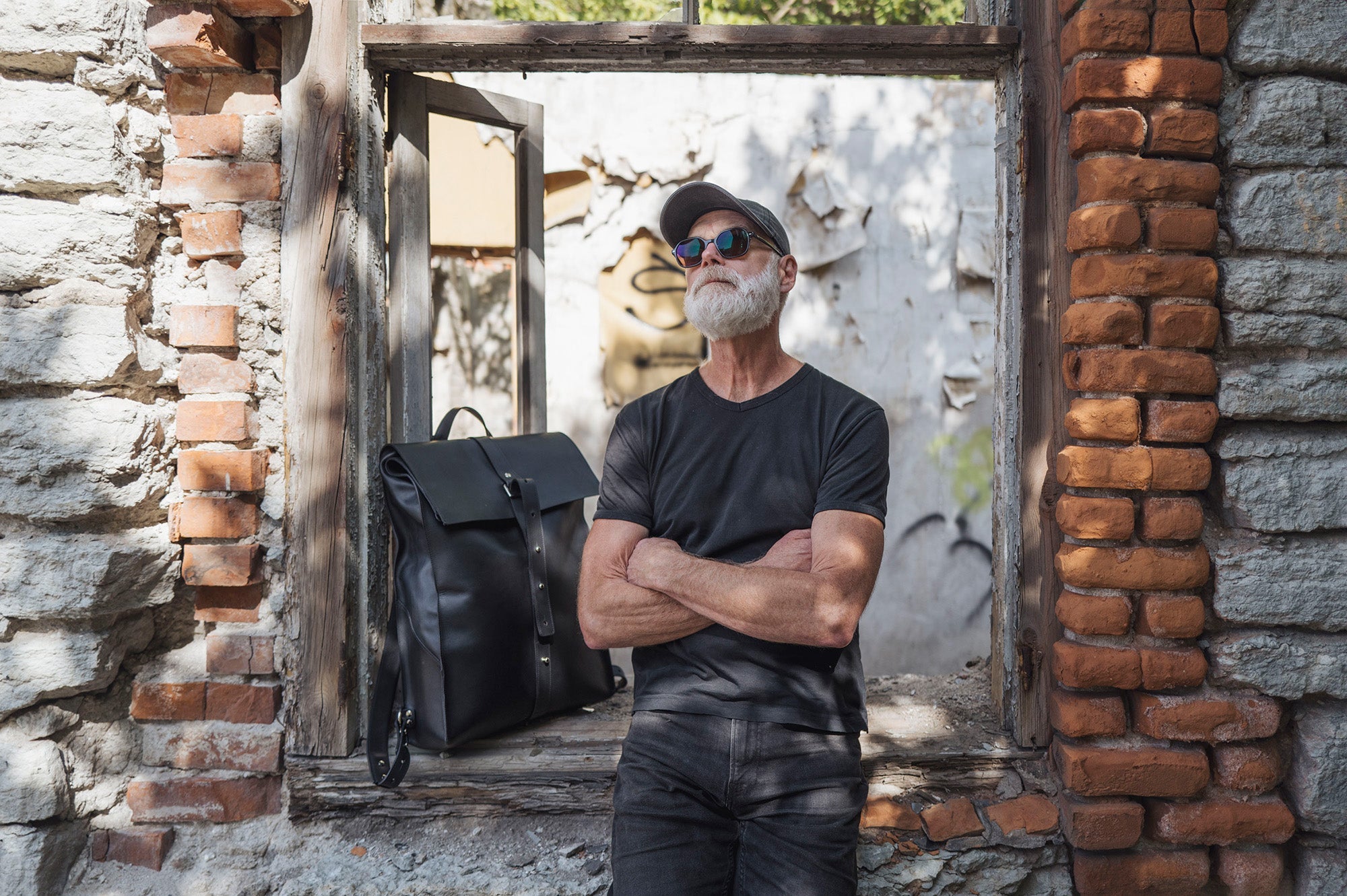 Man in a black t-shirt by a brick wall with a black Stella Soomlais leather backpack