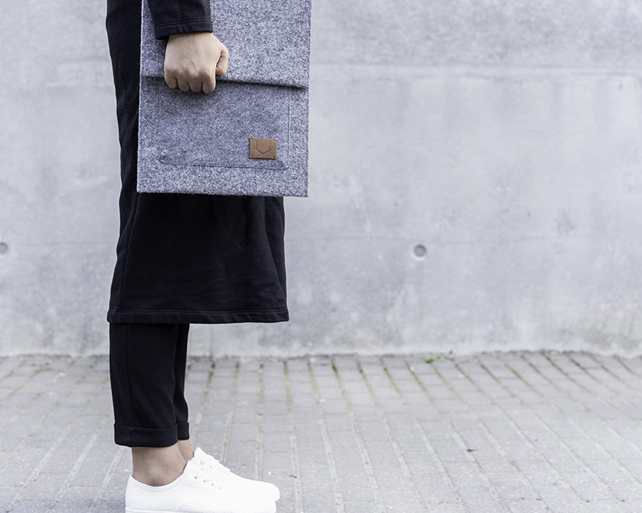 Grey recycled felt Malmö laptop sleeve by Nordhale, handmade in Estonia, carried against a concrete wall