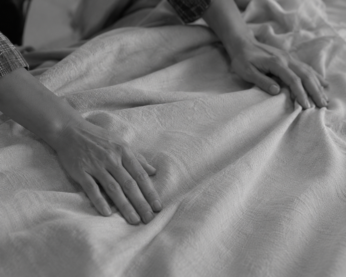 Two hands smoothing a textured woven throw on a bed, in black and white