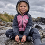 Girl in a pink and navy fleece lined rain set by Lenne, sitting on rocks by the sea