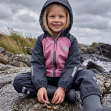 Girl in a pink and navy fleece lined rain set by Lenne, sitting on rocks by the sea