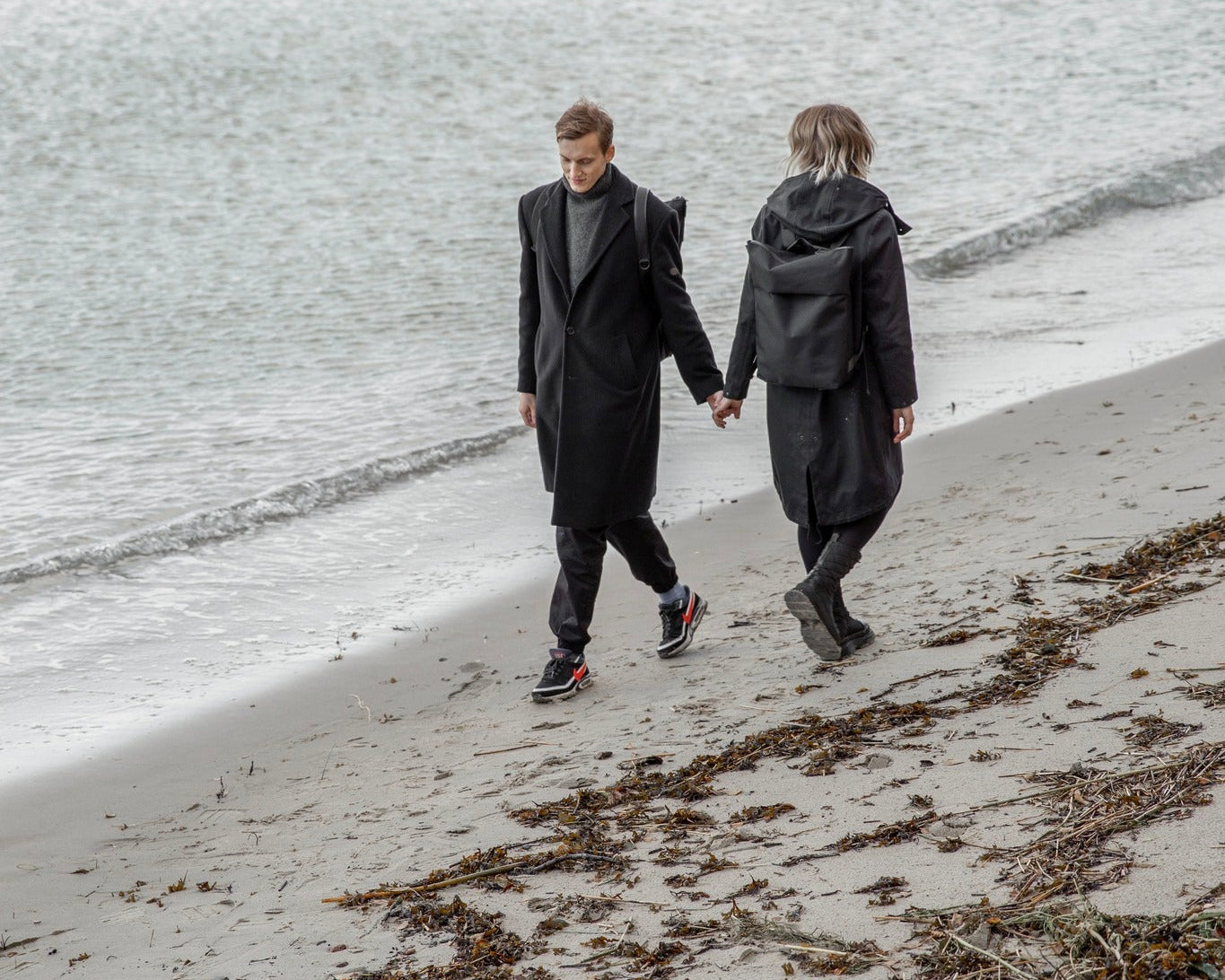 Couple walking on a Baltic beach, one wearing the Nordhale Hølar weatherproof backpack