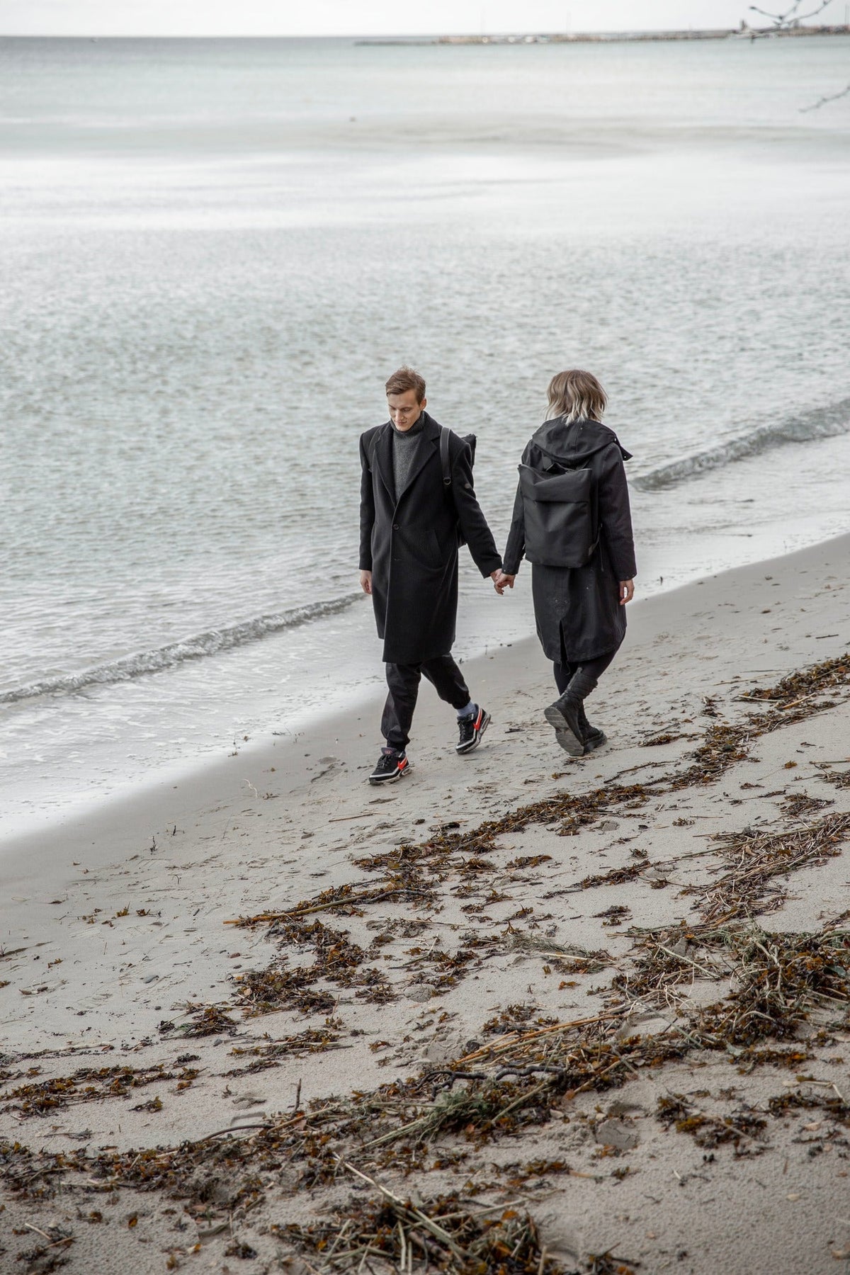 Et par går langs en strand ved Østersøen, den ene med Nordhales vejrbestandige rygsæk Hølar
