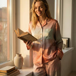 Tæwas Sunset silk pyjama set worn while reading a book by the window