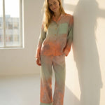 Tæwas Sunset silk pyjamas, button front shirt and drawstring trousers, worn leaning against a wall